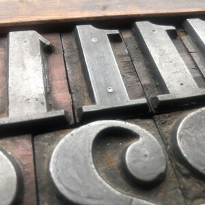 May include: Close-up of metal printing blocks with the numbers "111" and the letter "C" visible. The blocks are arranged in a row and are set in a wooden frame.