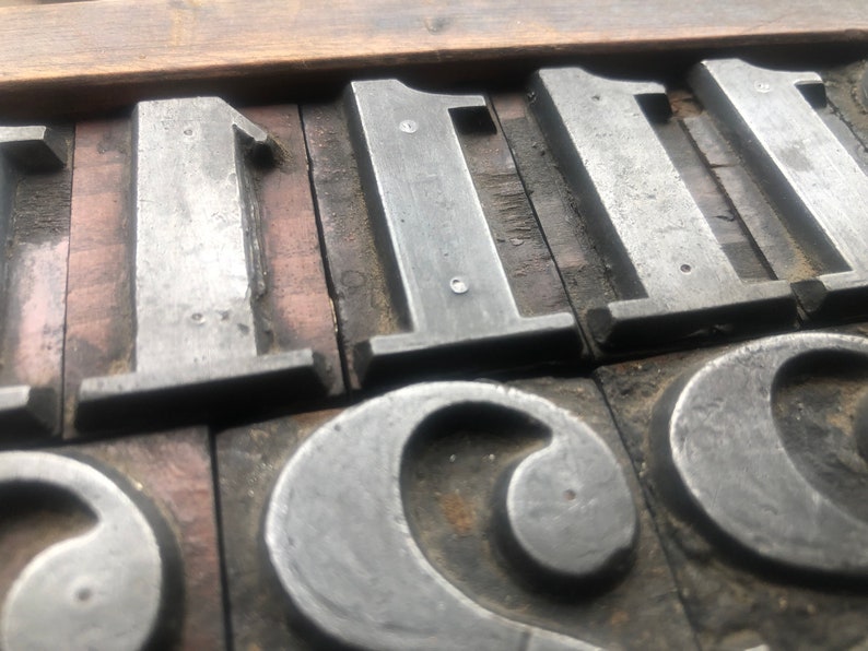 May include: Close-up of metal printing blocks with the numbers "111" and the letter "C" visible. The blocks are arranged in a row and are set in a wooden frame.