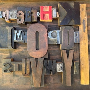 May include: A collection of vintage wooden and metal letterpress printing blocks featuring various uppercase letters, including a large red H and a prominent brown O. A wooden ruler measuring 30 cm is positioned vertically along the right side.
