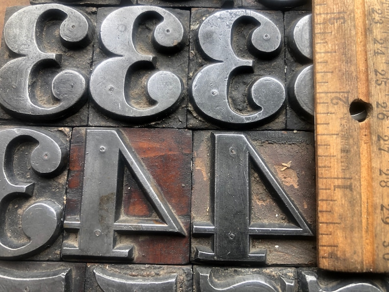 May include: Close-up of metal printing blocks with the numbers 333344. The blocks are arranged in a grid pattern and are set against a wooden background. A wooden ruler is visible on the right side of the image.