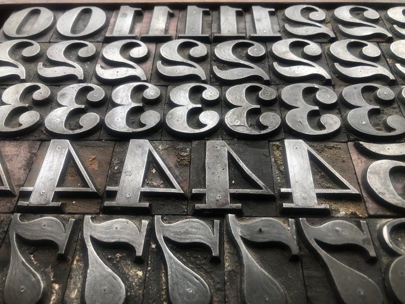 May include: Close-up of a collection of metal printing blocks, each with a different number engraved on it. The numbers include 0, 1, 2, 3, 4, and 7. The blocks are arranged in rows and columns, and the metal is worn and scratched from use.