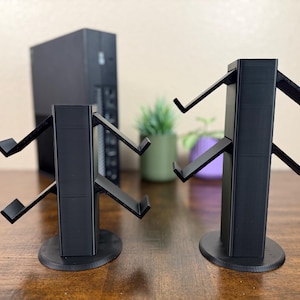 May include: Two black plastic stands with multiple arms for holding headphones. The stands are on a wooden surface.