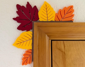 May include: A decorative corner accent featuring colorful fall leaves in shades of red, yellow, and orange. The leaves are arranged to frame a corner, adding a seasonal touch to home decor. The leaves are made of wood.