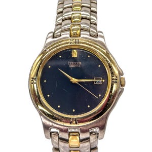 Puede incluir: Reloj de pulsera Citizen Quartz con una correa bicolor dorada y plateada y una esfera azul oscuro. El reloj tiene manecillas e indicadores de hora dorados, con una pantalla de fecha a las 3 en punto. Diseño clásico.
