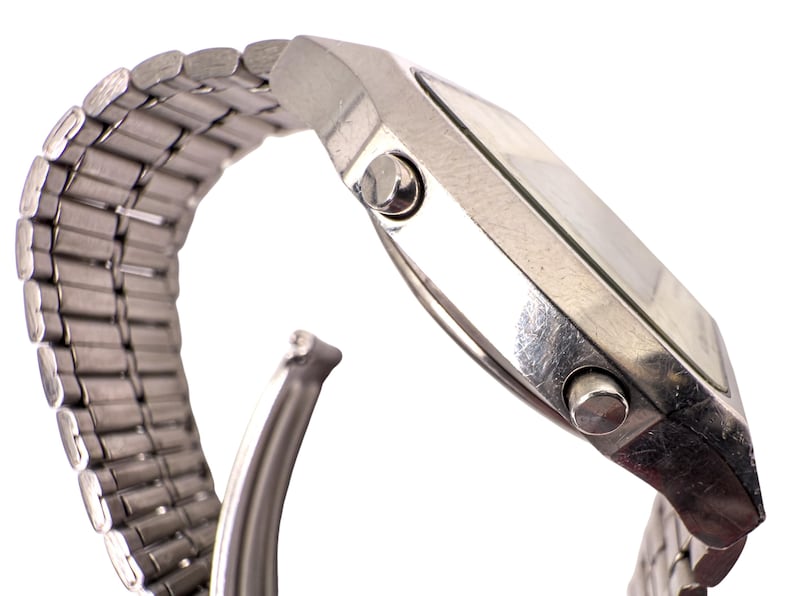 Puede incluir: Un reloj plateado con una esfera rectangular y una correa de metal con eslabones. El reloj tiene dos botones en el lateral y una fijaci&oacute;n de correa curvada. El reloj se muestra sobre un fondo blanco.