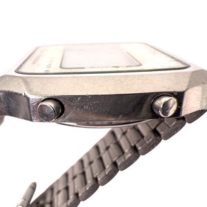 Puede incluir: Reloj digital plateado vintage con esfera rectangular y correa met&aacute;lica a juego. El reloj tiene dos botones laterales y una pantalla blanca. Un accesorio retro cl&aacute;sico.