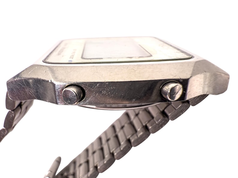 Puede incluir: Reloj digital plateado vintage con esfera rectangular y correa met&aacute;lica a juego. El reloj tiene dos botones laterales y una pantalla blanca. Un accesorio retro cl&aacute;sico.