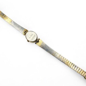 May include: A vintage Pierre Cardin wristwatch with a gold and silver-toned metal band. The watch face is round and features a small dial. The band is approximately 0.5 inches wide and tapers towards the clasp.