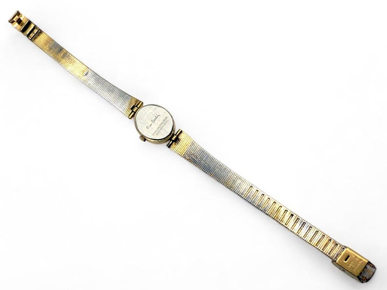 May include: A vintage Pierre Cardin wristwatch with a gold and silver-toned metal band. The watch face is round and features a small dial. The band is approximately 0.5 inches wide and tapers towards the clasp.