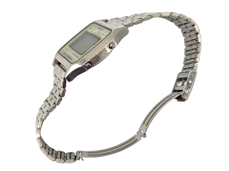Puede incluir: Un reloj de pulsera digital plateado con una pantalla rectangular y una correa de metal a juego. El reloj est&aacute; en &aacute;ngulo, mostrando la esfera y la correa flexible, que est&aacute; parcialmente desabrochada.