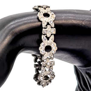 May include: A silver bracelet featuring a floral design, embellished with clear gemstones. The bracelet is made up of linked sections, each with a flower-like pattern and a central open circle. The gemstones provide a touch of elegance and sparkle.