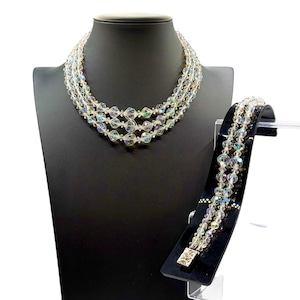 May include: A multi-strand iridescent crystal necklace and bracelet set. The necklace is on a black display stand and the bracelet is on a separate black stand.