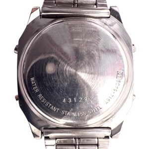 Puede incluir: Primer plano de la parte trasera de un reloj de acero inoxidable. La esfera del reloj es circular con un acabado de metal cepillado. El texto incluye "WATER RESISTANT STAINLESS STEEL" y el n&uacute;mero "431292".