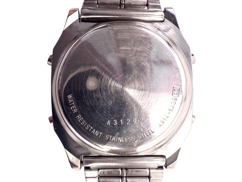 Puede incluir: Primer plano de la parte trasera de un reloj de acero inoxidable. La esfera del reloj es circular con un acabado de metal cepillado. El texto incluye "WATER RESISTANT STAINLESS STEEL" y el n&uacute;mero "431292".