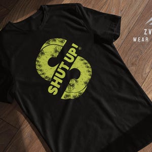 Könnte beinhalten: Schwarzes T-Shirt mit einer gelben Grafik von zwei Schallplattenspielern mit dem Text "SHUT UP!" darauf.