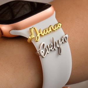 May include: A white Apple Watch band with two gold and silver name charms that say "Diana" and "Evelyn".