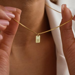 May include: A gold chain necklace with a small rectangular pendant featuring the letter "H" engraved on it.