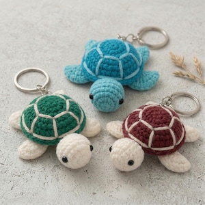 Puede incluir: Tres llaveros de tortuga de ganchillo en tonos verde, azul y burdeos. Cada tortuga tiene una barriga y detalles blancos, con un llavero plateado. Las tortugas están hechas a mano y tienen ojos de cuentas negras.