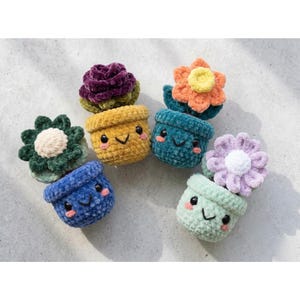 Puede incluir: Una colección de seis macetas de flores de ganchillo de colores con caras sonrientes. Cada maceta es de un color diferente, incluyendo azul, amarillo, verde azulado y verde, y está rematada con una flor de ganchillo en tonos de púrpura, naranja y verde. Las macetas están dispuestas sobre una superficie gris claro.