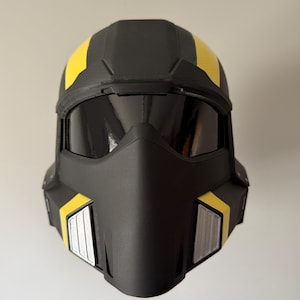 May include: A black helmet with yellow accents and a dark visor. The helmet has a streamlined design with a prominent face mask and rectangular details on the sides. The helmet appears to be made of a durable material.