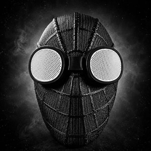 Op de afbeelding: Een zwart-wit afbeelding van een Spider-Man masker. Het zwarte masker heeft een webstructuur en grote, ronde, wit omrande ogen met een geperforeerd ontwerp. De achtergrond is donker en rokerig.