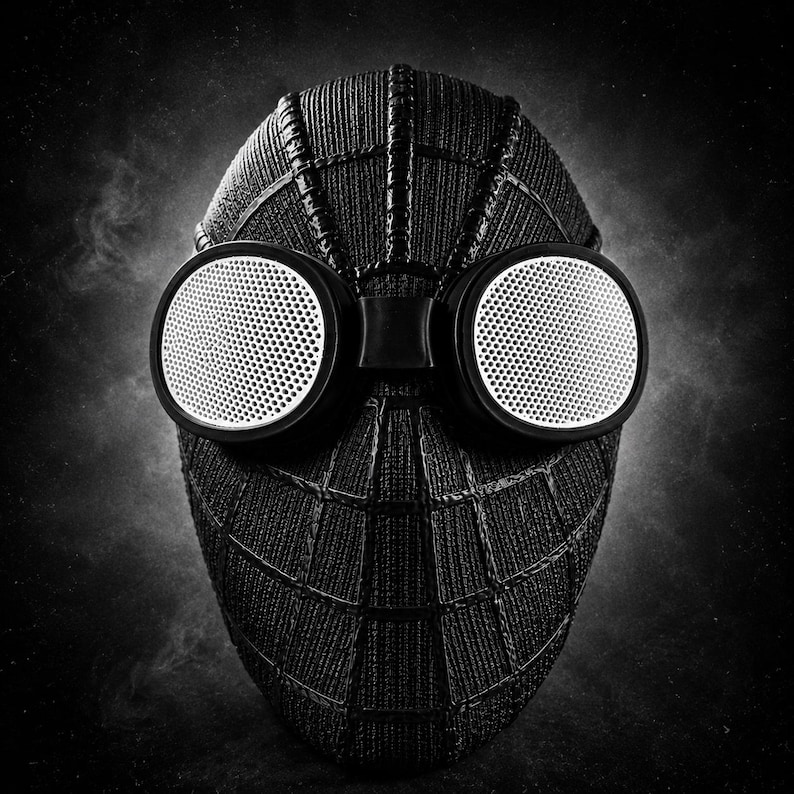 Op de afbeelding: Een zwart-wit afbeelding van een Spider-Man masker. Het zwarte masker heeft een webstructuur en grote, ronde, wit omrande ogen met een geperforeerd ontwerp. De achtergrond is donker en rokerig.