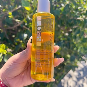 May include: A clear bottle of Terramar 3-in-1 hair oil, held in a hand. The bottle has a white cap and contains a yellow liquid. The label includes text in English and Spanish, mentioning macadamia and Tahitian Monoi oil extracts. The bottle contains 120 ml.