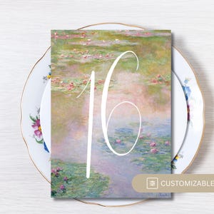 Pode incluir: Um cartão de número de mesa com uma pintura de nenúfares ao estilo Monet e o número 16 em branco. O cartão está sobre um prato floral, com rodelas de limão. O cartão está rotulado como "PERSONALIZÁVEL".