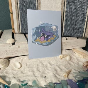 May include: A purple and blue cartoon creature with a large, round head and a small, pointed mouth is trapped inside a clear cube. The cube is surrounded by a white background with sparkles.