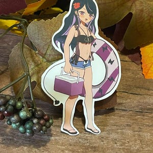 May include: A sticker of a cartoon woman with purple hair wearing a black bikini and a purple and white striped inner tube. She is holding a purple cooler and has a red flower in her hair.