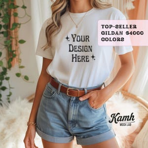 May include: A white Gildan 64000 t-shirt with the text "Your Design Here" in a distressed font. The model is wearing denim shorts and a brown belt. The image also includes the text "Top-Seller Gildan 64000 Colors" and "Kamh Mock Lab".