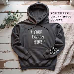 May include: A dark gray hooded sweatshirt with the text "YOUR DESIGN HERE" printed in white on the front and sleeve. The sweatshirt has a front pocket and a drawstring hood. The words "TOP-SELLER GILDAN 18500 COLORS" are in a pink box.