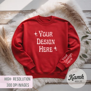 Peut inclure: Un sweat-shirt rouge avec l'inscription blanche "YOUR DESIGN HERE". La manche porte l'inscription "Your Design Here". Le sweat-shirt est pr&eacute;sent&eacute; sur une surface blanche et duveteuse.