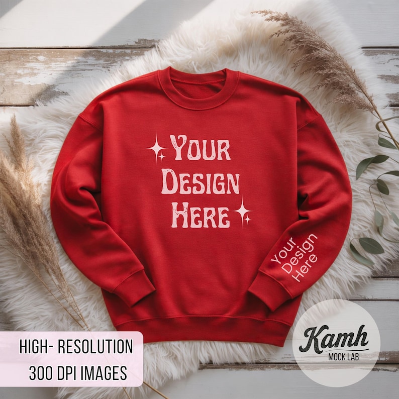 Peut inclure: Un sweat-shirt rouge avec l'inscription blanche "YOUR DESIGN HERE". La manche porte l'inscription "Your Design Here". Le sweat-shirt est pr&eacute;sent&eacute; sur une surface blanche et duveteuse.