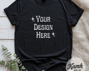 Könnte beinhalten: Schwarzes T-Shirt mit hochgekrempelten Ärmeln. Das Shirt zeigt den Text "YOUR DESIGN HERE" in weißer, stilisierter Schrift mit Sternen-Akzenten. Das Shirt wird auf einer weißen, fellartigen Oberfläche präsentiert.