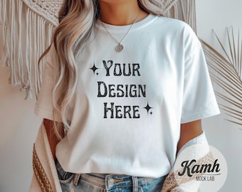 Könnte beinhalten: Weißes T-Shirt mit dem Text "YOUR DESIGN HERE" in schwarzer, Vintage-Schrift. Das kurzärmelige Shirt scheint aus einem weichen Material zu sein. Das Model trägt eine Jeans und eine Halskette. Im Hintergrund ist eine Wanddekoration zu sehen.