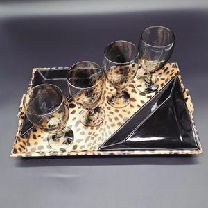 May include: A serving tray with a leopard print design, holding four wine glasses and two black serving dishes. The glasses have a matching leopard print pattern. The tray has a rectangular shape with a black border.