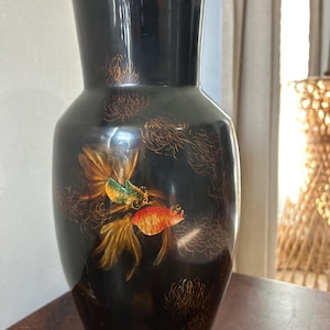 May include: Black vase with a glossy finish, featuring a hand-painted design of two goldfish in shades of orange, green, and gold. The vase has a wide base and a flared neck, with gold floral accents.