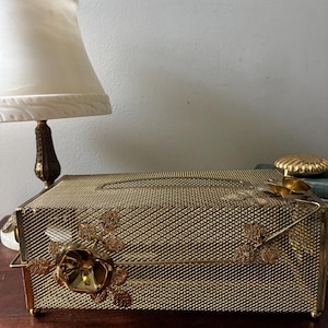 May include: A rectangular gold-tone metal tissue box cover featuring a fine wire mesh construction. The exterior is decorated with three-dimensional gold metal rose blossoms and textured leaves attached to the front and top surfaces.
