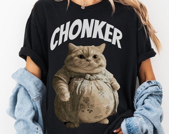 May include: A black t-shirt featuring a white graphic of a cat wearing a dress and the word "CHONKER" printed on it.
