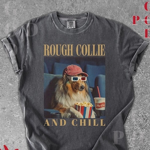 Op de afbeelding: Donkergrijs T-shirt met een Rough Collie met een 3D-bril en een pet, met popcorn en een drankje. De tekst "ROUGH COLLIE AND CHILL" staat boven en onder de afbeelding van de hond. Het shirt heeft opgerolde mouwen.