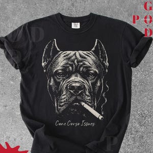 Könnte beinhalten: Schwarzes T-Shirt mit einer detaillierten Illustration eines Cane Corso-Hundes mit einer Zigarette im Mund. Der Text "Cane Corso Issues" ist unter dem Bild des Hundes aufgedruckt. Das T-Shirt hat hochgekrempelte Ärmel.