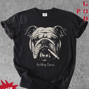 May include: Black t-shirt featuring a detailed illustration of a bulldog with a cigarette in its mouth. The design is in shades of white and gray, with the text "Bulldog Issues" below the image. The shirt has a classic crew neck.