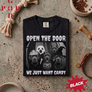 Könnte beinhalten: Ein schwarzes T-Shirt mit einer Grafik von vier Hunden in Halloween-Kostümen. Der Text lautet OPEN THE DOOR WE JUST WANT CANDY. Ein Hund trägt eine Eishockeymaske, einer ist ein Geist, einer ein Vampir und einer trägt einen Hexenhut mit Kürbiseimer.