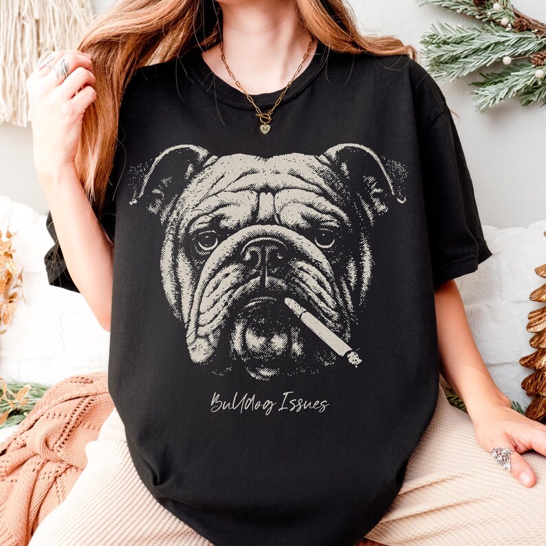 May include: Black t-shirt featuring a detailed illustration of a bulldog with a lit cigarette. The bulldog is in a neutral color, and the text "Bulldog Issues" is below the image.