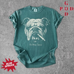May include: Teal-colored t-shirt featuring a detailed graphic of a bulldog with a cigarette in its mouth. The text "Bulldog Issues" is printed below the image. The shirt has rolled-up sleeves and a crew neck.