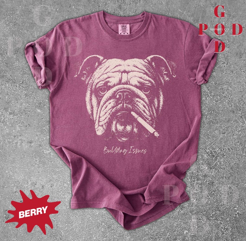 May include: Berry-colored t-shirt featuring a graphic of a bulldog with a cigarette. The bulldog's face is in a light beige color, and the text "Bulldog Issues" is below the image. The shirt has a crew neck and short sleeves.