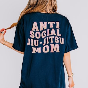May include: A dark blue t-shirt with a pink and white graphic that says "Anti Social Jiu-Jitsu Mom".
