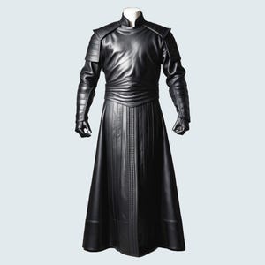 Pode incluir: Um traje de couro preto com uma longa túnica fluida e uma gola alta. O traje tem um cinto e uma série de linhas verticais na frente.