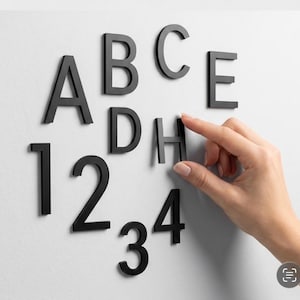 May include: A collection of matte black, three-dimensional letters and numbers including A, B, C, D, E, H, 1, 2, 3, and 4. These individual characters feature a clean, sans-serif typeface and are arranged in a scattered layout on a flat surface.